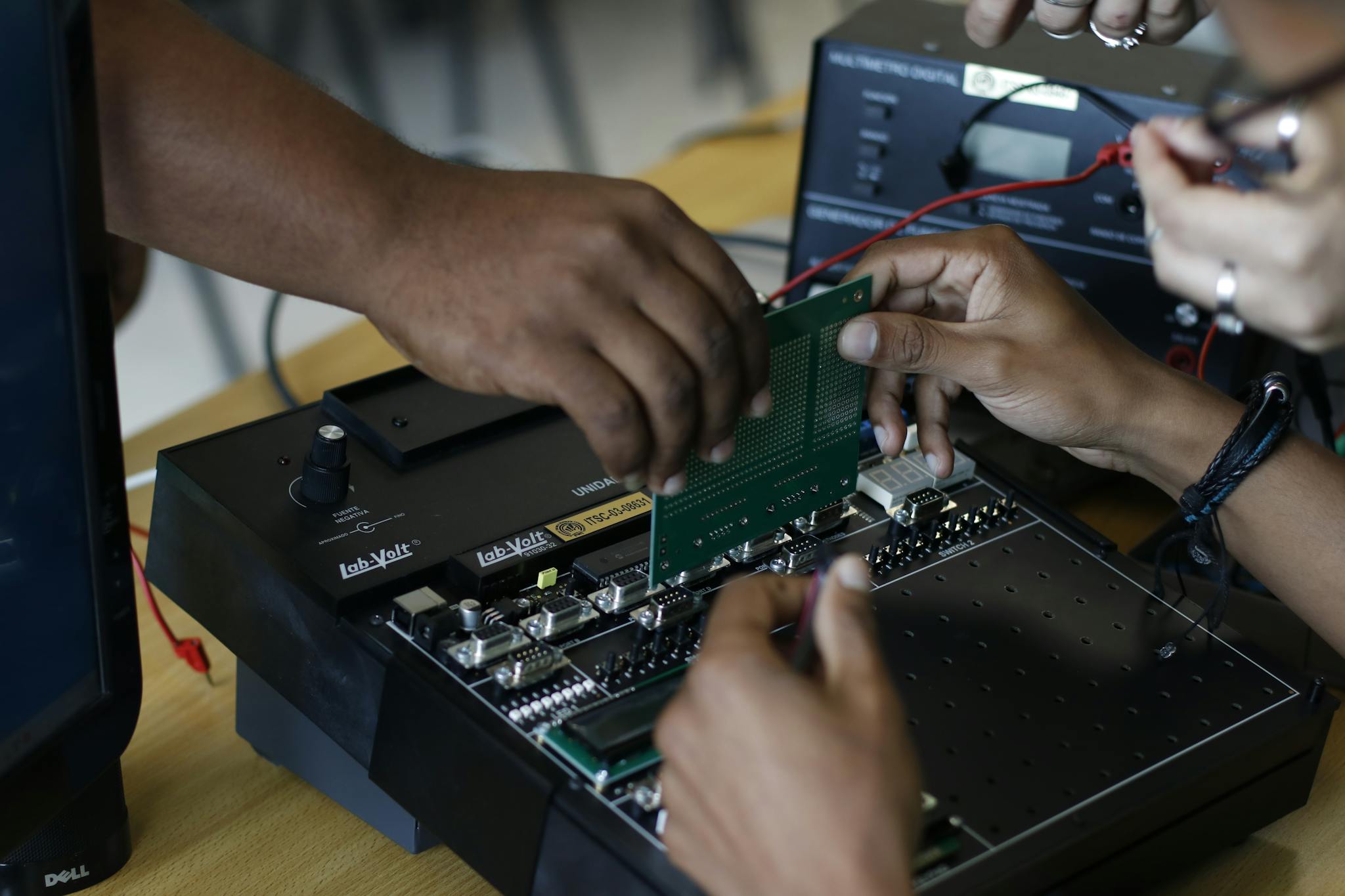 Close-up of hands assembling an electronic circuit board, showcasing teamwork and technical expertise.