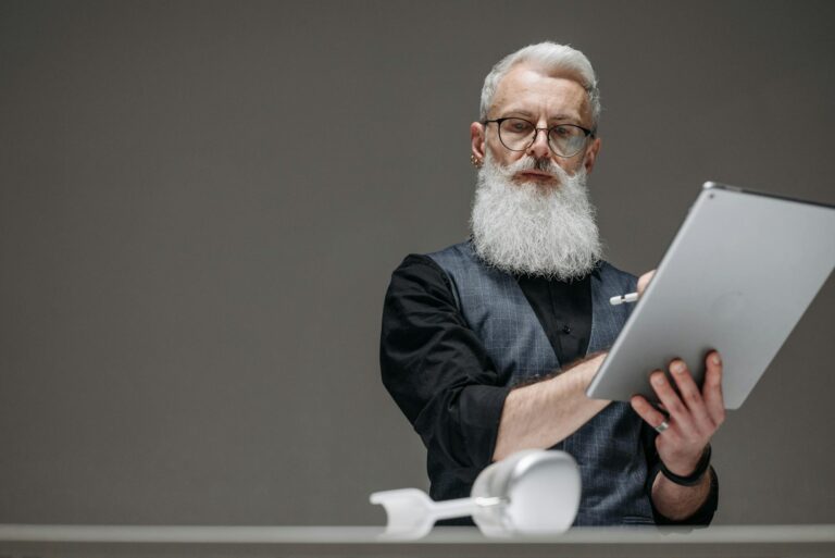 Bearded senior man in black long sleeves using a tablet, illustrating innovation and technology.