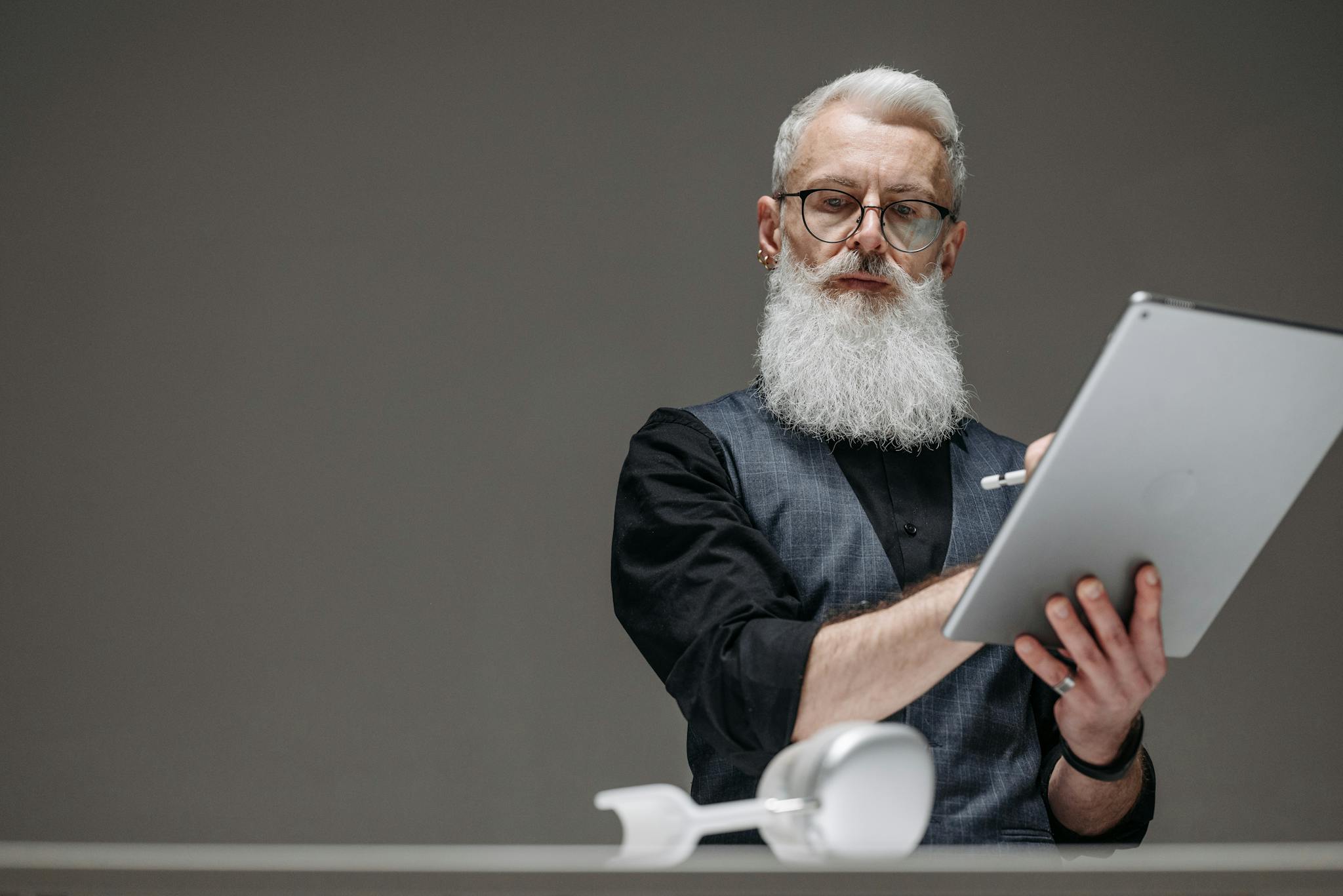 Bearded senior man in black long sleeves using a tablet, illustrating innovation and technology.