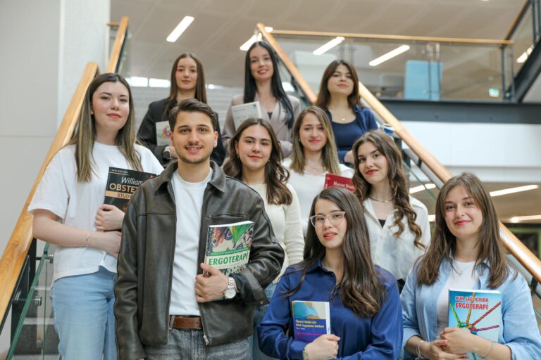 Diverse group of students smiling on stairs, holding educational books indoors.