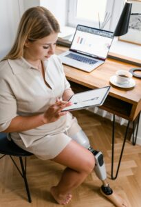 Woman with a prosthetic leg works on a tablet in a modern home office setting.