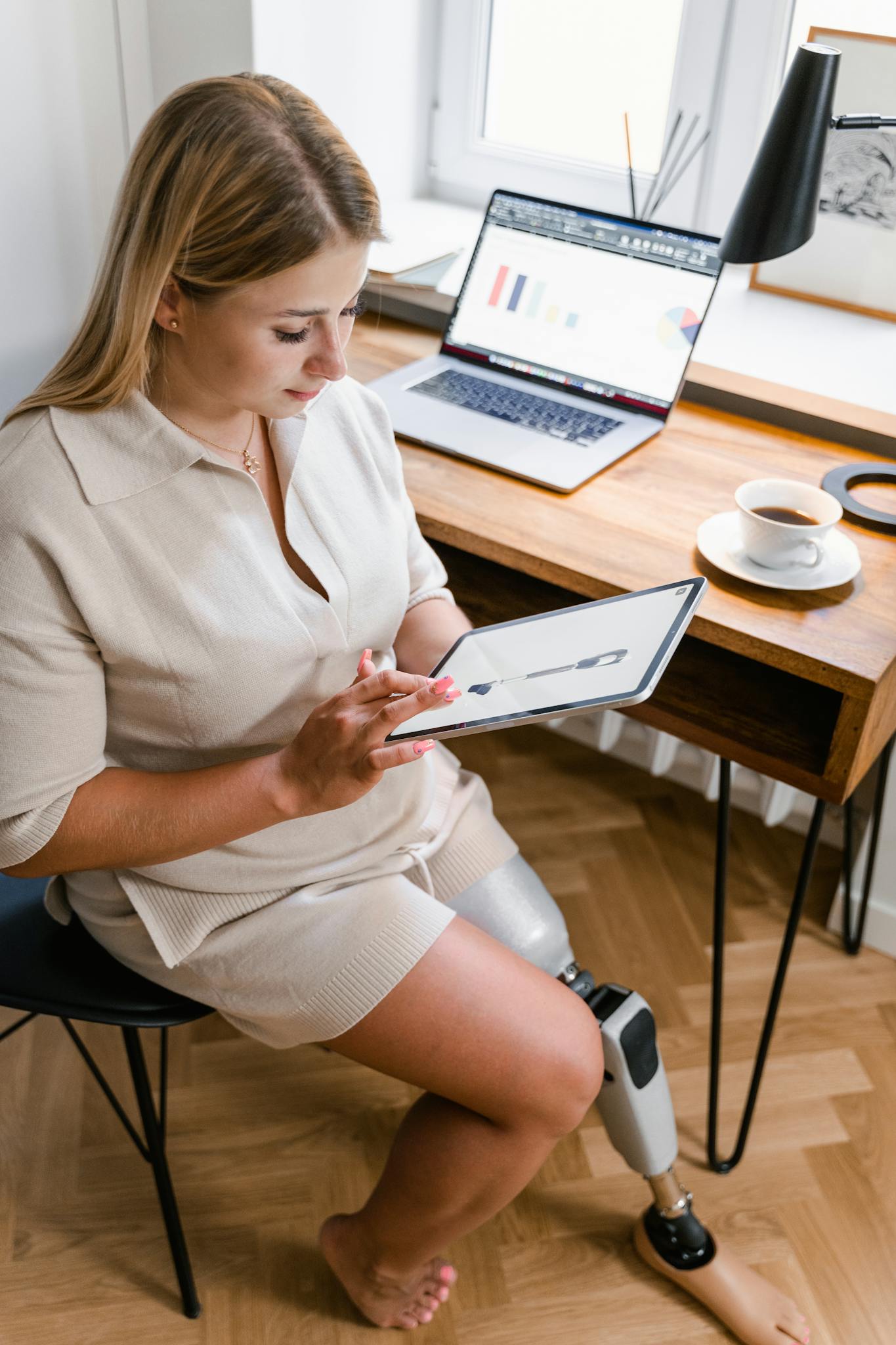Woman with a prosthetic leg works on a tablet in a modern home office setting.