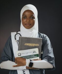 Young female healthcare graduate holding books in studio portrait.